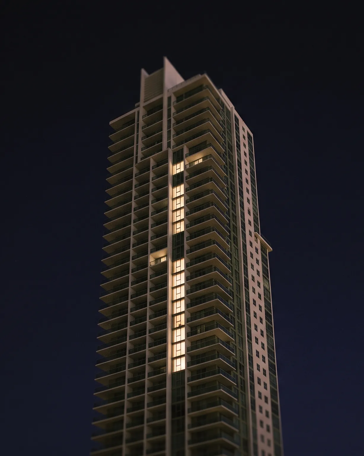 Modern luxury condominium tower at night with a column of lit windows