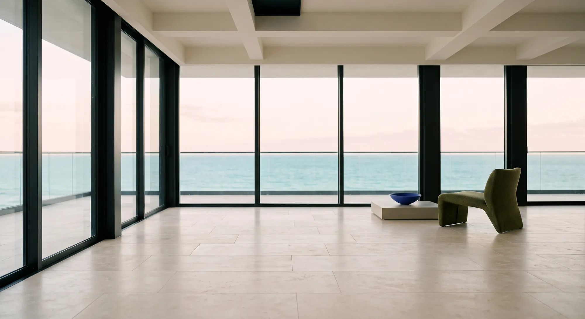 Empty oceanfront luxury residence with floor-to-ceiling windows and an olive lounge chair